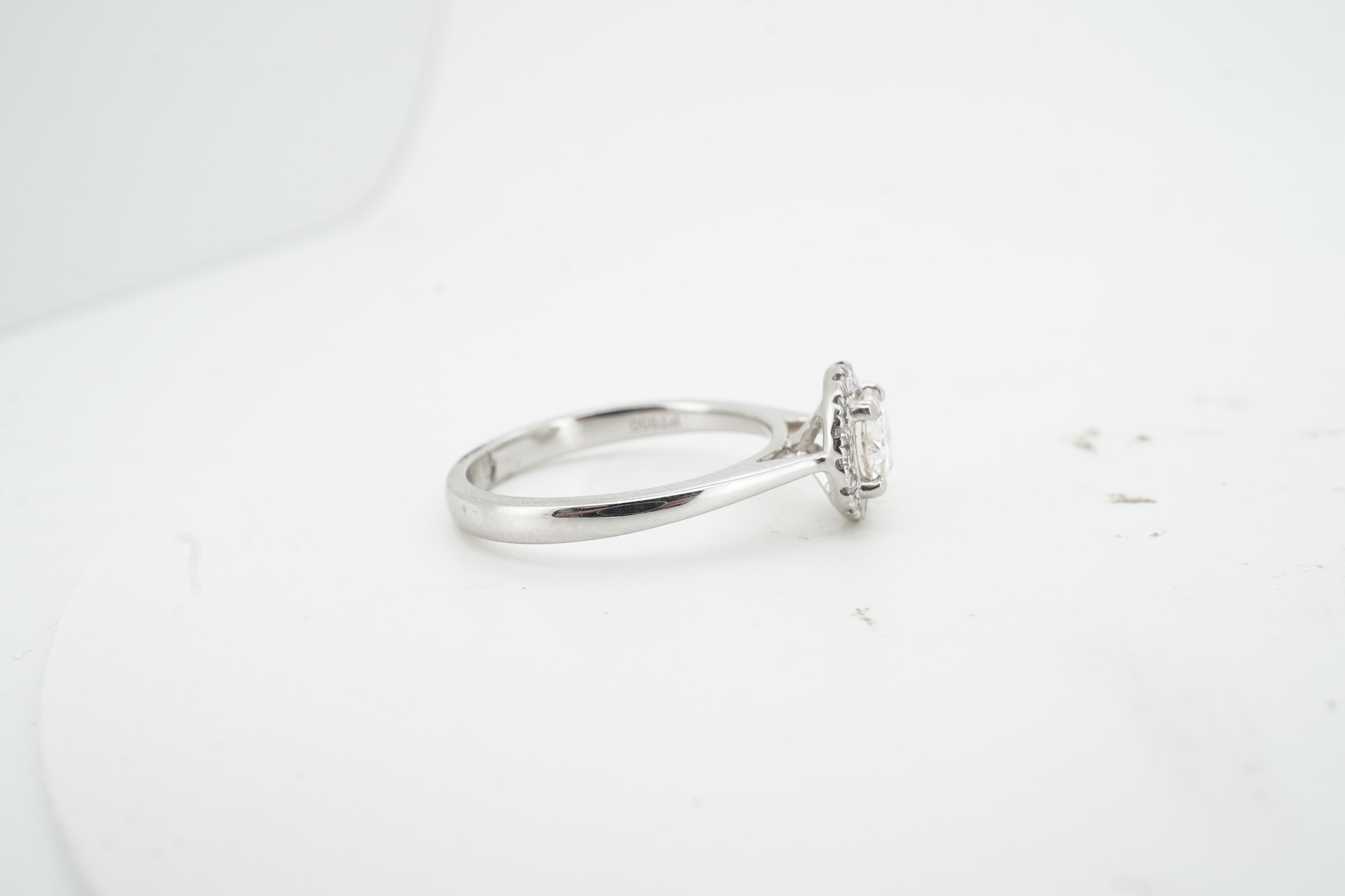 A diamond cluster ring, claw-set with a brilliant-cut diamond weighing approximately 0.70 carats, within a border of smaller brilliant-cut diamonds totalling approximately 0.10 carats, mounted in platinum, size M, Britis